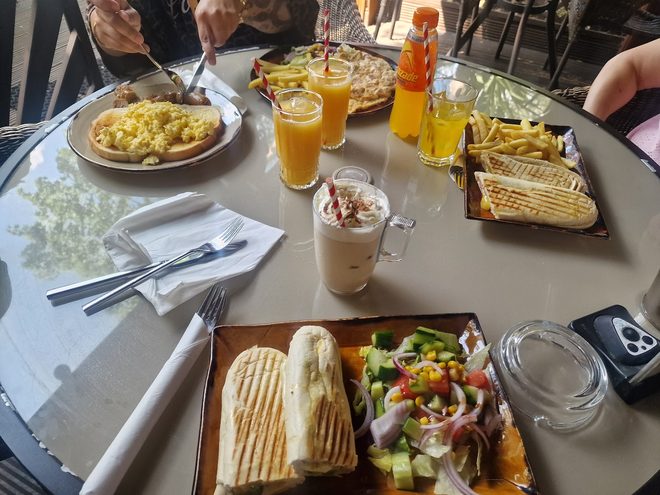 A shared table mid-meal with panini, salad, eggs and orange juice