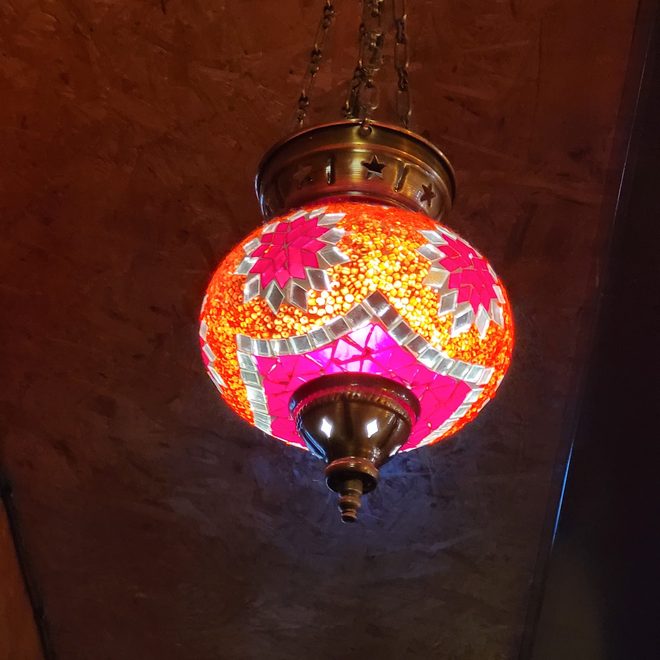 Glowing orange and pink mosaic lamp close against a dark ceiling