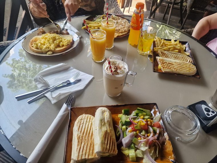 Panini with salad and scrambled eggs on a shared table with orange juice